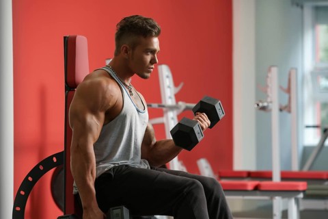 Handsome young man training with dumbbells in gym