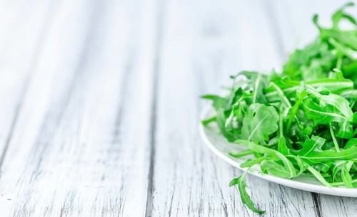 Wooden table with fresh Arugula as detailed close-up shot (selective focus)