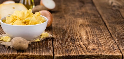 Cheese and Onion Potato Chips on an old wooden table as detailed close-up shot (selective focus)