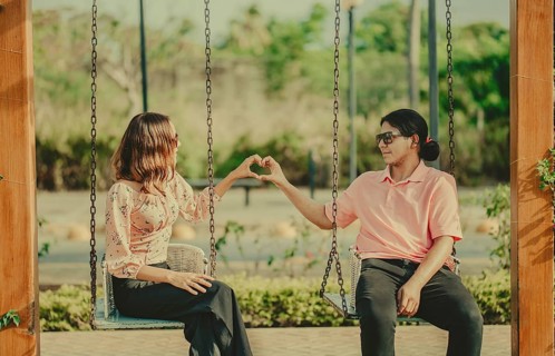 Young couple in love sitting on a swing making a heart shape. Happy couple in love on a park swing