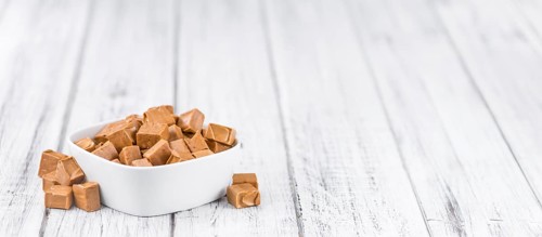 Caramel pieces as high detailed close-up shot on a vintage wooden table (selective focus)
