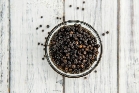 Preserved black Peppercorns on a wooden table as close-up shot