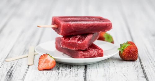Old wooden table with homemade Strawberry Popsicles (close-up shot, selective focus)