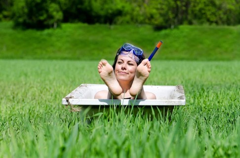 Happy Woman with a Diving Mask Lying in a Bathtub on the Green Field and Showing Her Feet in a