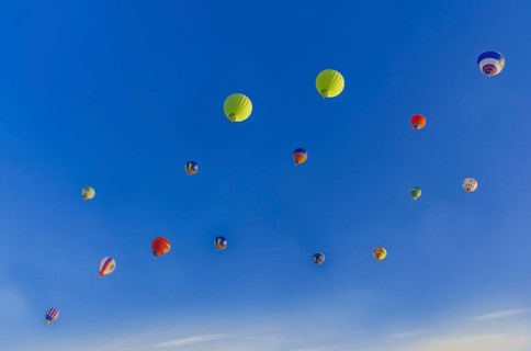Colorful hot air balloons floating in a clear blue sky with a few clouds, creating a vibrant and