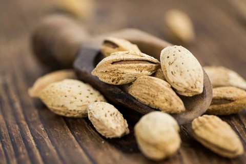 An old wooden table with roasted Almonds (in the shell) as detailed close-up shot (selective focus)