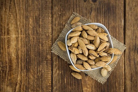 An old wooden table with roasted Almonds (in the shell) as detailed close-up shot (selective focus)