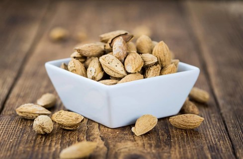 An old wooden table with roasted Almonds (in the shell) as detailed close-up shot (selective focus)