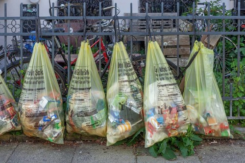 Yellow bags for plastic waste, hanging on a garden fence in front of a house entrance, waste