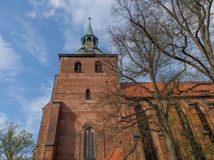 Impressive Gothic-style brick church tower surrounded by trees under a partly cloudy sky, lüneburg,