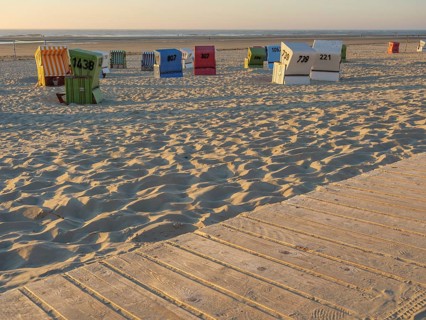 A wooden promenade leads past colourful beach chairs on the quiet sandy beach, langeoog, germany