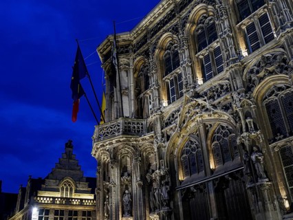 Monumental historic building with detailed facades and flags against a dramatic evening sky, Ghent,