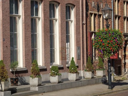 Facade of a brick building with large windows and plants in pots and a hanging flower basket,