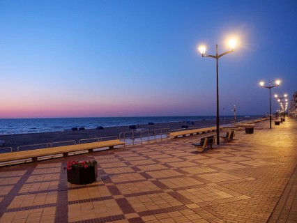 An empty promenade at dusk, illuminated by lanterns, the sea in the background, a peaceful and