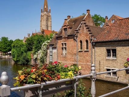 A canal with decorated balustrades and flowers along the row of brick-built houses in front of a
