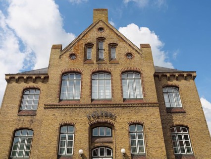 Large, multi-storey brick building with numerous windows and a clear sky, Kappeln,
