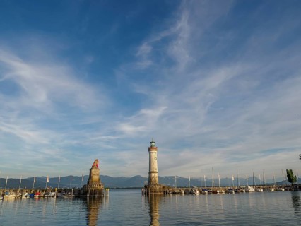 A harbour with a lighthouse and a fisherman's statue, surrounded by boats and mountains in the