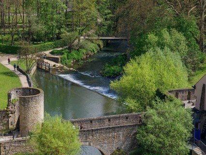 A river with a bridge and ruins in the middle of a green park landscape, walkers enjoying nature,