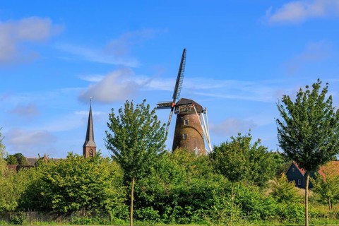 Landscape with windmill and church tower, surrounded by green trees and blue sky, bredevoort,