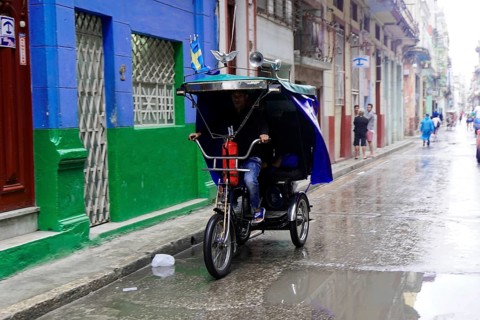 Havana, Cuba, Central America, man riding a cycle rickshaw on a wet road in an urban environment,