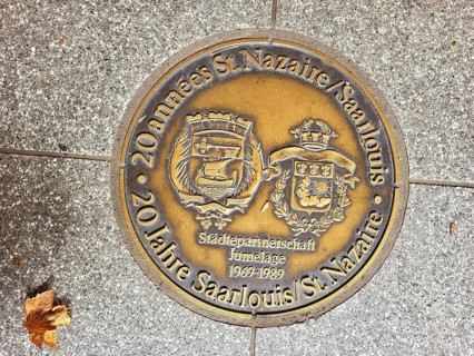 Bronze plaque embedded in a pavement. The plaque is in German and reads '20 Jahre St. Nazaire