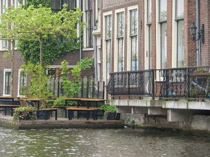Urban canal with neighbouring buildings and metal balcony balustrades, next to tables and chairs by