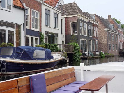 A boat moored in front of a row of townhouses on the canal on a calm, cloudy day, windows with