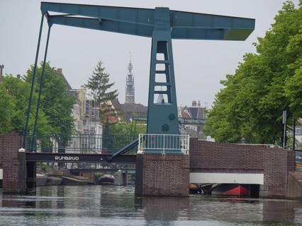A bascule bridge over a canal with a church tower in the background and tree-lined streets, Leiden,