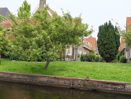 A well-kept lawn with trees and houses along a quiet canal, peaceful and green surroundings,
