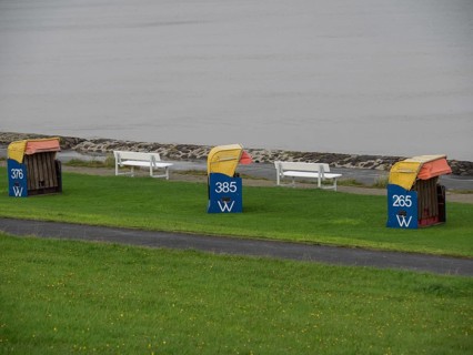 Three colourful beach chairs and white benches on a green lawn, quiet coastal atmosphere under a