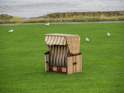 A single beach chair on a green meadow near the sea, surrounded by birds, cuxhaven, germany