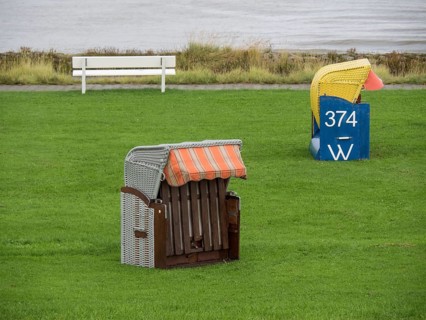 A single beach chair and a bench stand on a green meadow by the sea, cuxhaven, germany