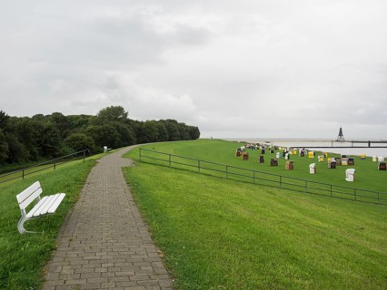 A paved path and a bench lead to a meadow with colourful beach chairs, cuxhaven, germany