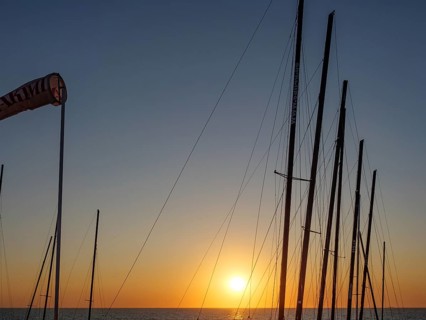 Sunset over the sea with silhouettes of sailboat masts in a peaceful atmosphere, De Haan, Flanders,