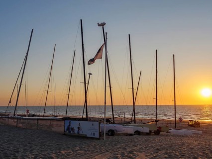 Boats with masts on the beach at sunset, calm atmosphere, warm light and sea in the background, De