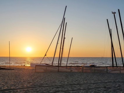 Beach with boat masts at sunset, calm and peaceful atmosphere, sand and sea, warm colours, De Haan,