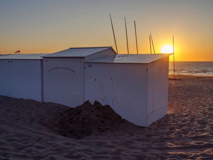 White painted beach huts on the beach at sunset with calm sea and sandy bottom, De Haan, Flanders,