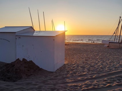 Sunset on the beach with white huts and a boat, warm colours and a calm atmosphere, sea in the
