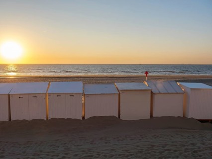 Beach with white huts, sunset over the sea, warm orange colours and calm atmosphere, De Haan,