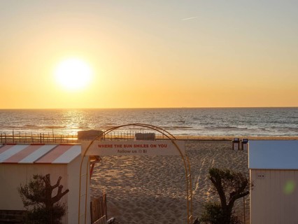 Sunset over the sea, beach with sand and an archway with lettering, quiet and peaceful atmosphere,