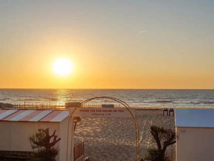 Sunset on the beach, quiet atmosphere, an archway with lettering, sea in the background, trees on