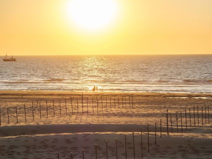 People on the beach at sunset, with a ship in the background, De Haan, Flanders, Belgium, Europe