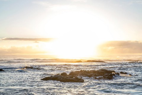Sunrise over the sea with gentle waves. Sandy beach with lava rocks and blue water alternating with