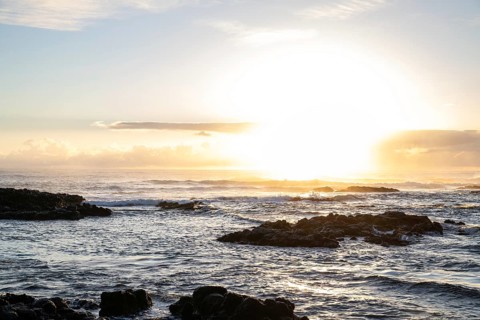 Sunrise over the sea with gentle waves. Sandy beach with lava rocks and blue water alternating with