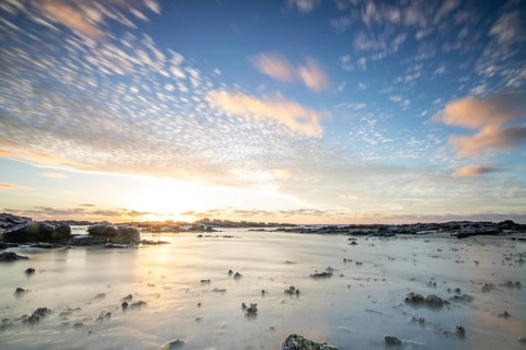 Sunrise over the sea with gentle waves. Sandy beach with lava rocks and blue water alternating with