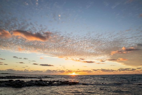 Sunrise over the sea with gentle waves. Sandy beach with lava rocks and blue water alternating with