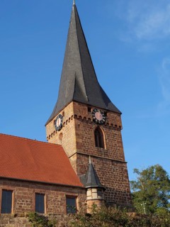 Historic church with a high tower and visible bells. Traditional architecture under a blue sky,