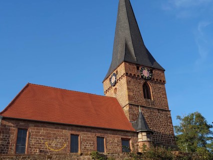 Historic church with high tower and bells. Brick walls with a red roof under a clear sky, Kandel,