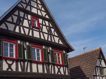 Two historic half-timbered houses with windows and colourful shutters under a blue sky, Kandel,