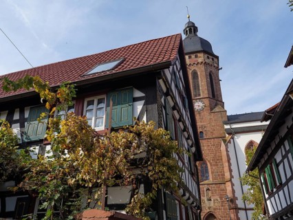 A half-timbered house with green shutters and autumnal vines next to a church, Kandel, Palatinate,